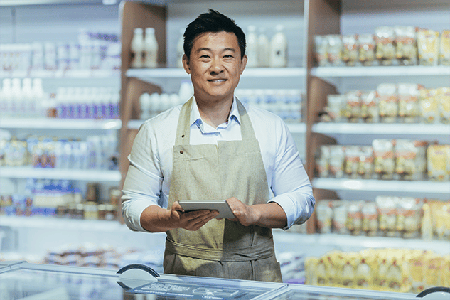 Asian man facing the camera smiling holding tablet while standing in a storefront