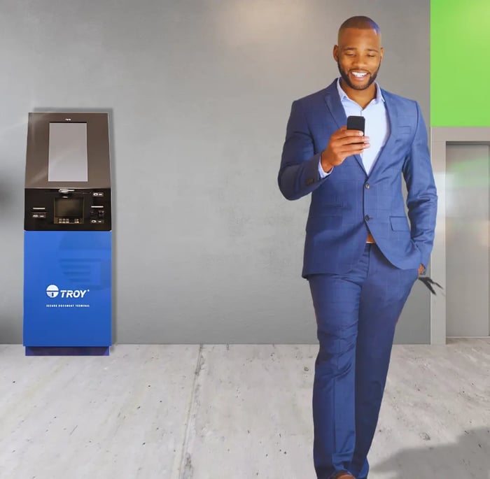 Man with blue suit walking away from TellerCentral Machine while looking at phone