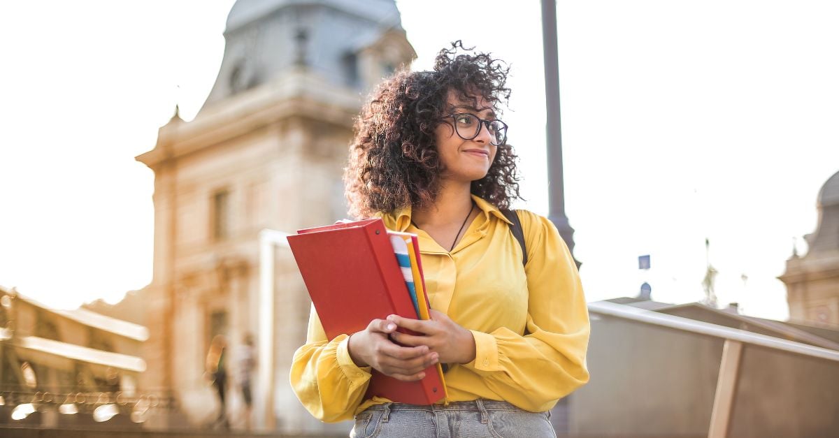 Female student holding books in front of college building 