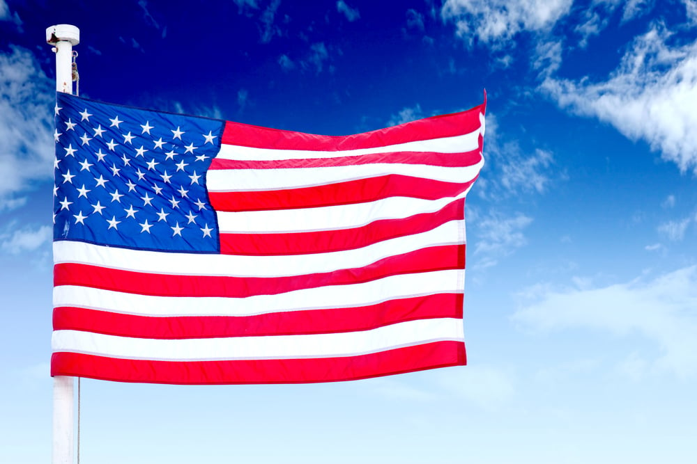 Picture of the the American flag waves in the wind with blue sky in  the background 