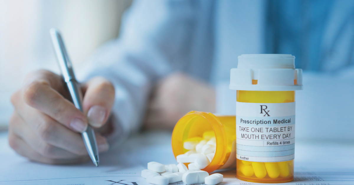 Person writing prescription with medication sitting on desk